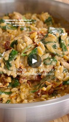 a pan filled with pasta and spinach on top of a wooden table next to a knife