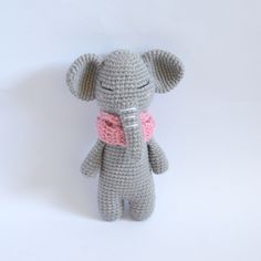 a crocheted gray elephant with a pink bow on it's neck sitting in front of a white background