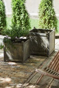 two wooden planters sitting next to each other on a brick patio with trees in the background