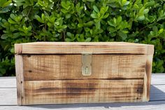 a wooden box sitting on top of a table next to some bushes and trees in the background