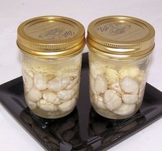 two jars filled with garlic sitting on top of a black square plate next to each other