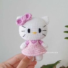 a crocheted hello kitty doll in a pink dress is held up to the camera