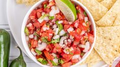 a white bowl filled with salsa surrounded by tortilla chips and lime wedges