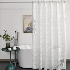 a white shower curtain in a bathroom next to a bathtub and table with flowers