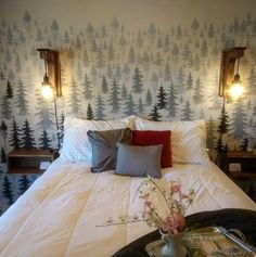 a bed with white sheets and trees on the wall next to two night stands that have lights on them