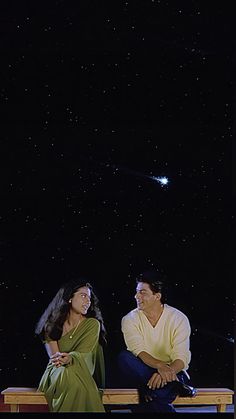 a man and woman sitting on a bench looking at the stars