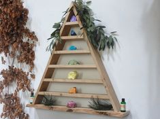 a triangle shaped shelf with plants and rocks on the top, hanging from a wall