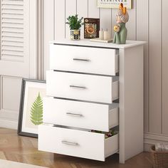 a white dresser with three drawers and pictures on the wall next to it in a room