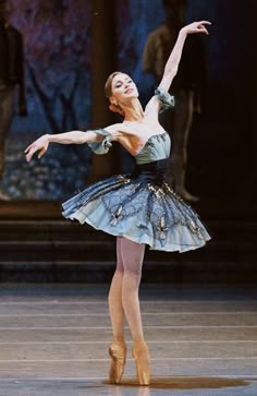 the ballerina is wearing a blue dress and has her arms outstretched in the air