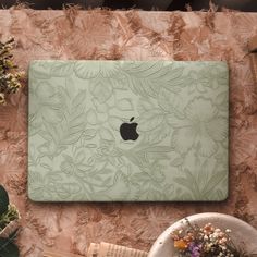 an apple laptop sitting on top of a table next to some flowers and other items