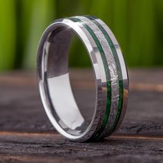 a wedding band with green and silver inlays sits on top of a piece of wood