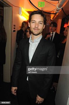 a man in a suit standing next to a wall with people behind him at an event