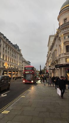 a red double decker bus driving down a street next to tall buildings