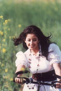 a woman riding on the back of a bike down a road next to tall grass