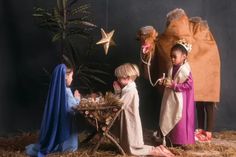 three children dressed up as nativity scene with baby jesus in manger, star and tree