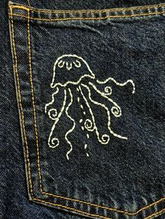 an embroidered octopus on the back pocket of a pair of blue denim jeans with yellow stitching