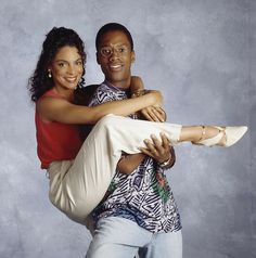 a man and woman are posing for a photo in front of a gray background with their arms around each other