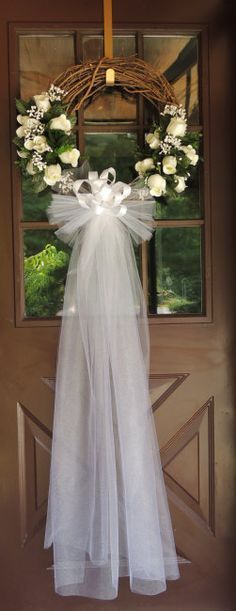 a wreath hanging on the front door with white flowers and ribbon tied around it's bow