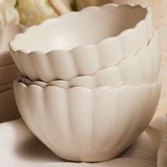 three white bowls sitting next to each other on top of a table with flowers in the background