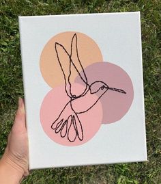 a hand holding up a piece of paper with a drawing of a hummingbird on it