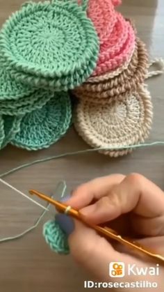 two hands are crocheting the ends of several coasters on a wooden table