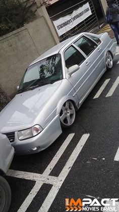 a silver car parked on the side of a road next to a curb with people walking by