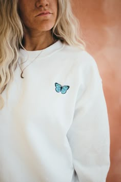 a woman wearing a white sweatshirt with a blue butterfly embroidered on the back of it