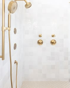 a shower with gold fixtures and white tiled walls in a bathroom, including two hand held shower heads