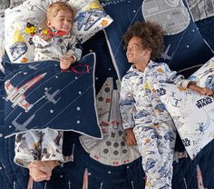 two children laying in bed with star wars themed sheets and pillowcases on them