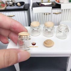 a person is holding some miniature jars in front of a small table with other items on it