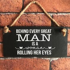 a sign that says behind every great man is a woman rolling her eyes on a brick wall