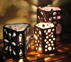 three lit candles sitting on top of a wooden table next to each other with holes in them