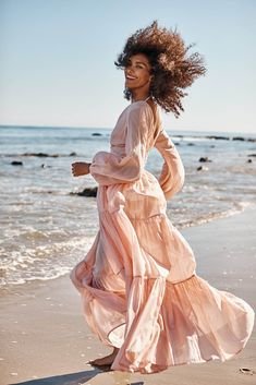 a woman in a pink dress is running on the beach with her hair blowing in the wind