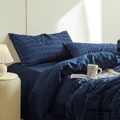 a bed with blue sheets and pillows in a bedroom next to a lamp on a table