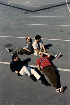 three men laying on the ground in an empty parking lot with their feet up against each other