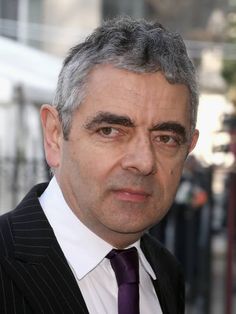 a close up of a person wearing a suit and tie with grey hair in the background