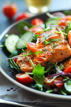 a salad with salmon and tomatoes on a plate next to a glass of wine in the background