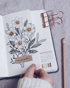 an open notebook with flowers drawn on it next to a pencil and some other items