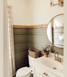 a white toilet sitting next to a sink in a bathroom under a large round mirror