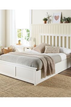 a white bed sitting on top of a wooden floor next to a dresser and window