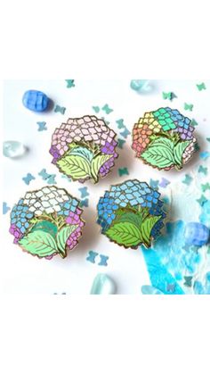 four different colored brooches sitting on top of a white table next to confetti