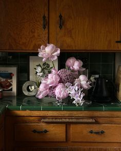 some flowers are sitting on top of a counter in a room with wooden cabinets and green tile