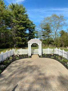 a white fenced in area with flowers on the ground and a gazebo at the end