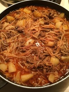 a skillet filled with meat and noodles on top of a stovetop next to other cooking utensils