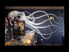 an octopus painted on the side of a wall next to a glass case with food in it