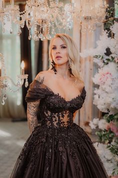 a woman wearing a black dress standing in front of a chandelier and flowers