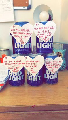 four beer cans with hearts on them sitting on a desk next to an open book