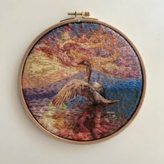 a needle - embroidered picture of a bird in the water with a sunset behind it