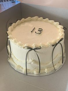 a white cake in a box with the number thirteen on it's top and ribbon around the edges