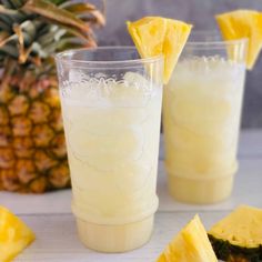 two glasses filled with pineapple juice next to sliced pineapples